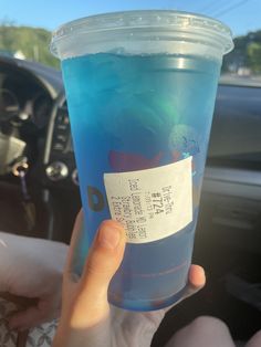 a person holding up a blue drink in their hand with a ticket attached to it