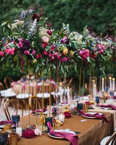 a long table topped with lots of purple and red flowers next to tall gold candles