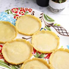 four small pies on a colorful plate next to a coffee cup and potted plant