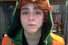 a young man with red hair wearing a green hoodie in front of a bookshelf