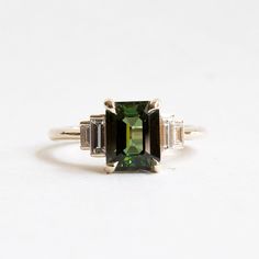 an emerald and diamond ring with three baguets on the side, set in white gold