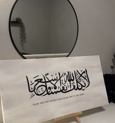 an arabic calligraphy is displayed in front of a mirror on a table with a wooden easel