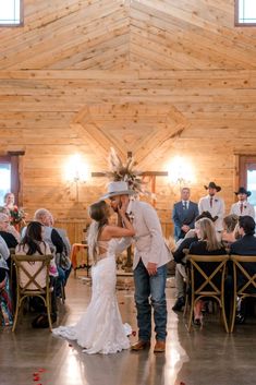 a bride and groom kissing in front of an audience at their wedding reception, surrounded by wooden walls