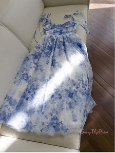 Regal and refined, this blue floral homecoming dress is a stunning choice for any special occasion. The dress is adorned with a delicate blue floral print that is both classic and contemporary, creating a look that is as elegant as it is fresh. The bodice features ruched detailing that enhances the bust and adds texture, while the off-the-shoulder straps with charming bow accents provide a feminine and romantic touch. The waist is cinched with a slender tie, allowing the full skirt to drape beau Floral Print Prom Dress For Prom Season, Chic Floral Print Dresses For Prom Season, Light Blue Floral Print Wedding Dress, Blue Sweetheart Neckline Midi Dress For Bridesmaid, Feminine Floral Print Dress For Prom Season, Sleeveless Floral Print Midi Dress For Prom, Feminine Floral Print Prom Dress, Fitted Floral Print Midi Dress For Bridesmaids, Blue Floral Print Dress For Prom Season