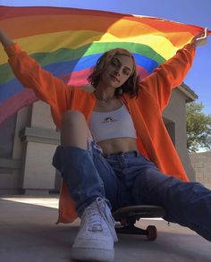 a woman sitting on top of a skateboard holding a rainbow flag