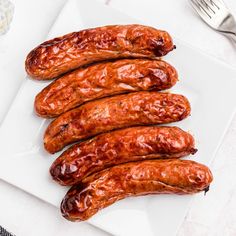 four sausages on a white plate next to a fork