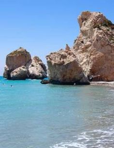 two large rocks sticking out of the ocean next to a beach with people swimming in it