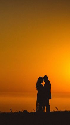 two people standing in front of the sun with their arms around each other and kissing