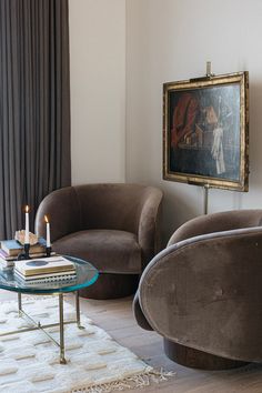 a living room with two chairs and a table in front of a painting on the wall