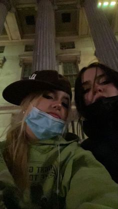 two women with face masks on taking a selfie in front of an old building