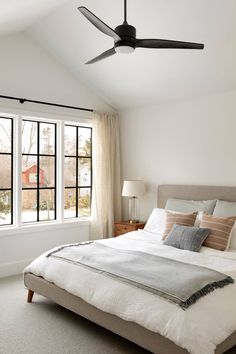 a bedroom with a bed, ceiling fan and two windows