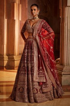 a woman in a red and gold lehenga standing on the floor with her hands on her hips