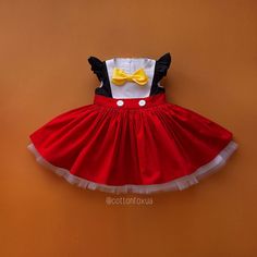 a red and white dress with a yellow bow on the back is hanging up against a wall