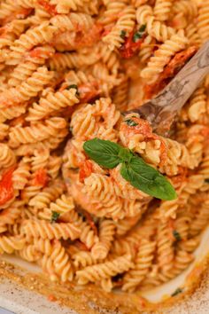 a pasta dish with tomato sauce and spinach leaves on a wooden spoon in the casserole dish