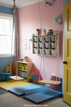 Bright and colorful children's playroom featuring two wooden swings, organized storage bins on the wall, and a soft play mat. The room is designed for fun and creativity, with toys and educational materials visible. Playground Room, Playroom Organization Ideas, Bedroom Concept, Small Playroom