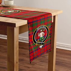 a red and green plaid table runner with the clan crest on it next to a wooden table