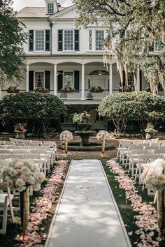 an outdoor ceremony setup with white chairs and pink flowers on the aisle in front of a large house