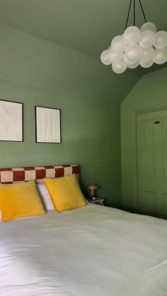 a bedroom with green walls and white bedding, two framed pictures on the wall