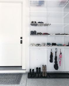 a white closet filled with lots of shoes and umbrellas next to a door that has a black mat on the floor