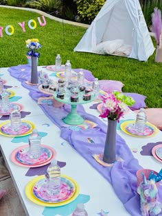 a table set up with plates, cups and vases on it in the grass