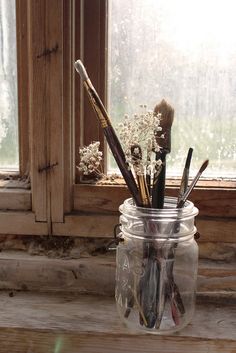 a jar filled with brushes sitting on top of a wooden table next to a window