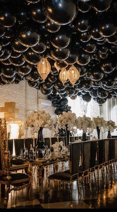 black and white balloons hang from the ceiling above a dining room table with gold chairs