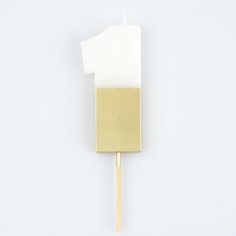 a gold and white toothpick sitting on top of a wooden stick in front of a white wall