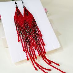 a pair of red and black beaded earrings on a white card with pink flowers in the background