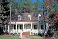 a white house with black shutters and red steps in front of the door is surrounded by trees