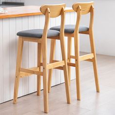 two wooden stools sitting next to each other on a kitchen counter with an island in the background