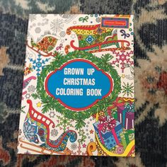 the grown up christmas coloring book is laying on top of a carpeted area with blue and red lettering