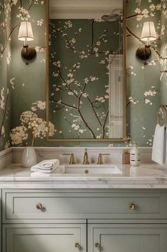 a bathroom with green wallpaper and white counter top, gold faucet lights