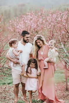 a family posing for a photo in front of some pink trees with blossoms on it