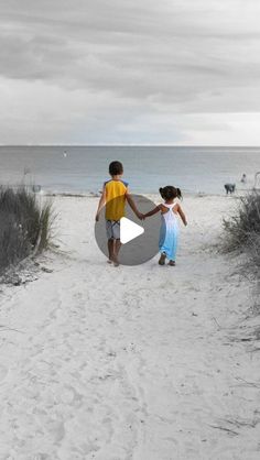 two children are walking on the beach with a surfboard