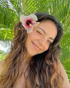 a woman with long brown hair and a flower in her hair smiling at the camera