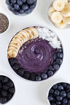 blueberry smoothie bowl with banana slices, bananas and other fruit in bowls on a white surface