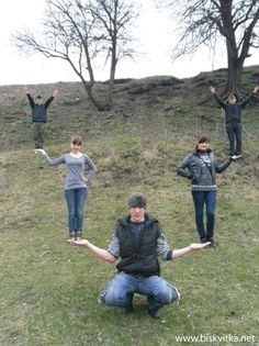 a group of people standing on top of a grass covered field with trees in the background