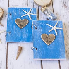 two blue notebooks decorated with starfish and seashells are sitting on a white wooden table