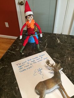 an elf sitting on top of a counter next to a note with a deer's head