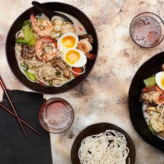 two black bowls filled with noodles and shrimp next to chopsticks on a table