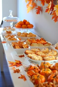 an assortment of baked goods are displayed on a long table with fall leaves hanging from the ceiling