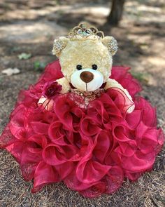 a teddy bear in a red dress sitting on the ground