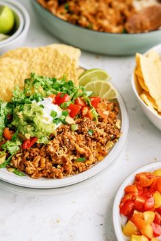 mexican food is served on white plates with lime wedges and tortilla chips