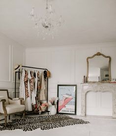 a room with a chandelier, chair and clothes on hangers in it