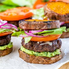 two hamburgers with lettuce, tomato and onion on top are sitting on wax paper