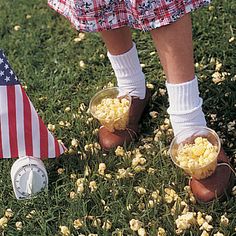 a person standing in the grass with some popcorn and an american flag behind her legs