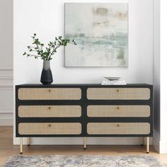 a black and beige dresser with two vases on it's sides next to a painting