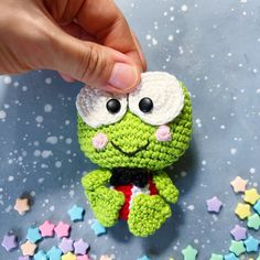 a crocheted green stuffed animal being held up by someone's hand with stars around it