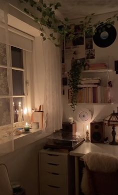 a room with a desk, window and plants on the wall next to it is lit by candles