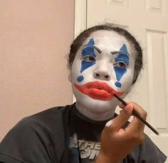 a man with his face painted blue and white, holding a paintbrush in front of his face